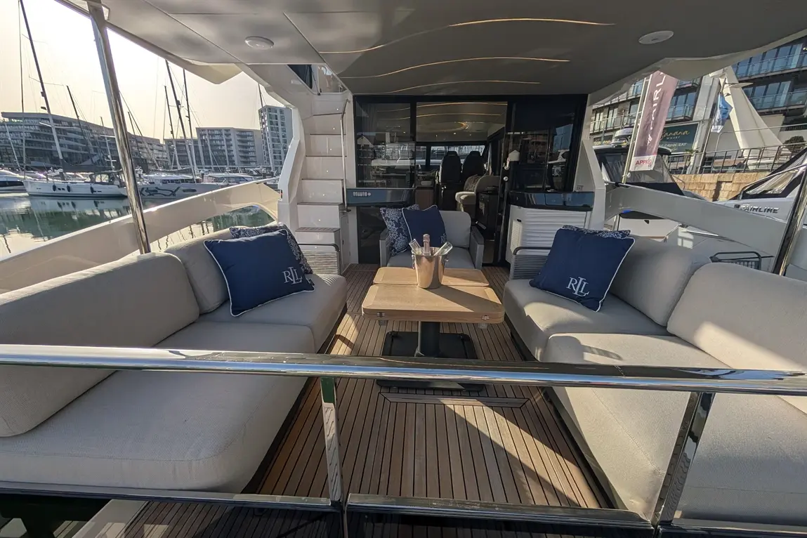 Stylish yacht interior featuring grey sofas with blue pillows, a wooden table, and marina views, ideal for relaxation.